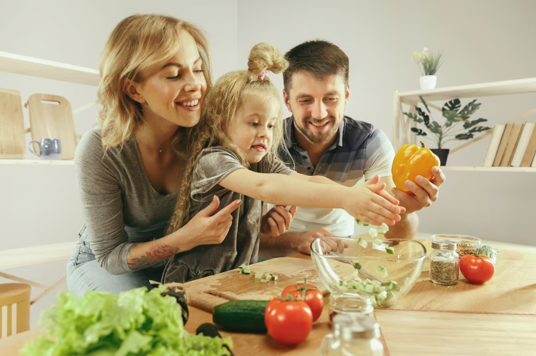 a little girl and her parents are cutting vegetables and smiling while making salad in the kitchen at home