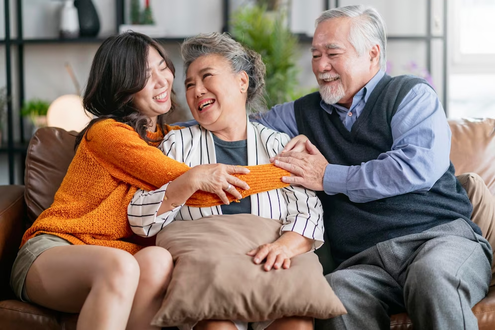 Image of a woman embracing her elderly mother, with her father standing beside them, and all of them sharing smiles