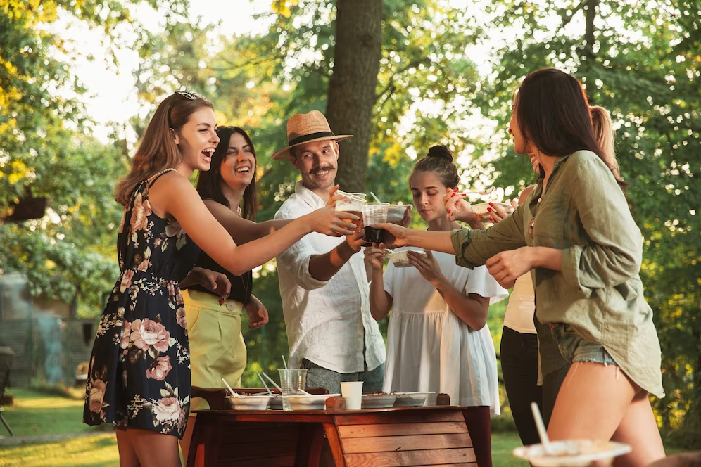 Image of a group of people outdoors, raising their glasses for a toast, surrounded by lush trees