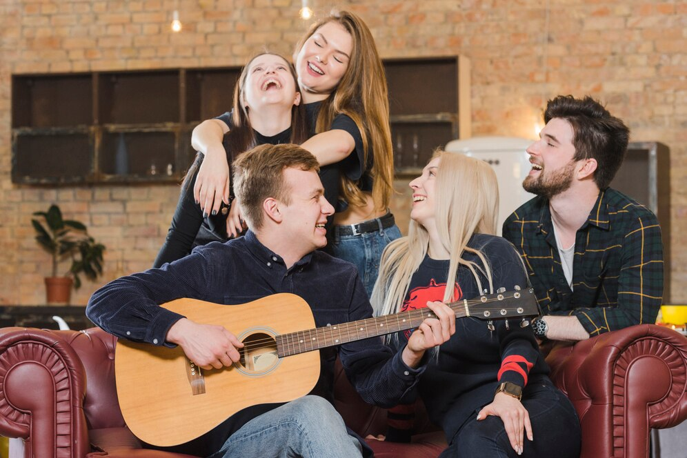 Image of a group of people sitting on a sofa, enjoying themselves and smiling, while one person plays the guitar.