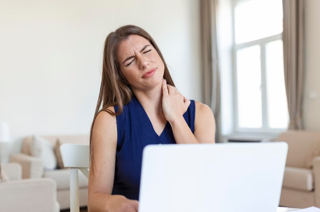 woman in dark blue blouse with closed eyes sitting in front of the opened laptop, the beige sofa behind her