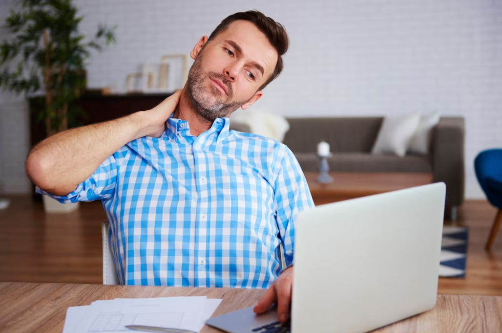 man in blue and white shirt holding his neck white watching on the laptop on the desk