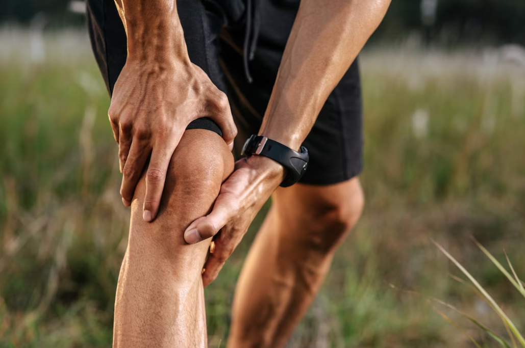 bent man in black shorts holds his knee and stands on the grass