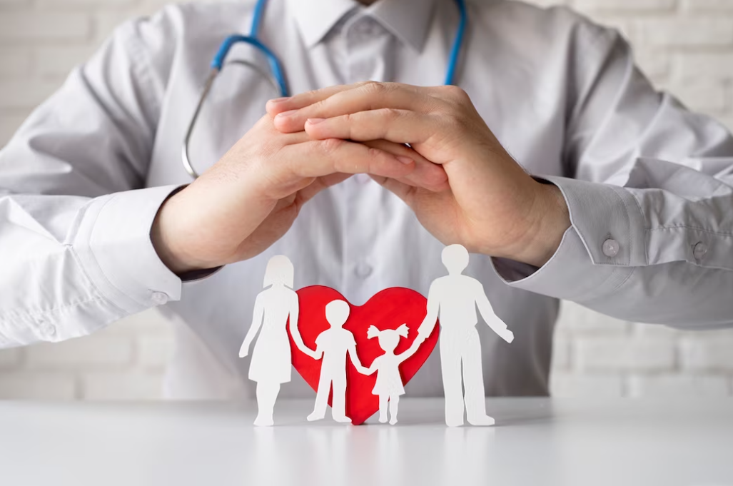 a doctor in white clothing sitting with hands on the table, the family paper figures and red heart on the table