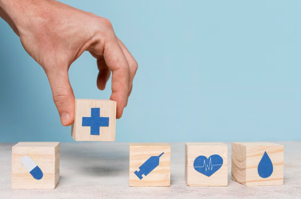 hand put a cube with a cross on it, other wooden cubes with healthcare sign on it on the table, the blue wall behind